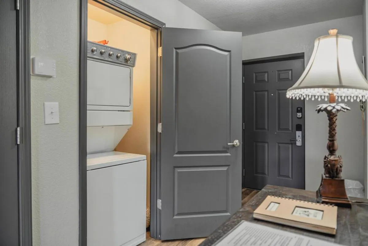 A functional laundry area featuring a stacked washer and dryer next to doorways and a cozy lamp-lit corner. The practical setup invites guests to keep clothes fresh throughout their stay, adding an extra layer of comfort.
