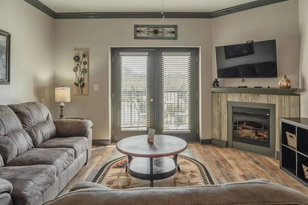 This image features a living area with comfortable sofas, a coffee table, a fireplace, and TV. Large sliding doors draw in natural light and offer a sense of connection to the outdoors, inviting guests to relax after a day exploring Pigeon Forge.