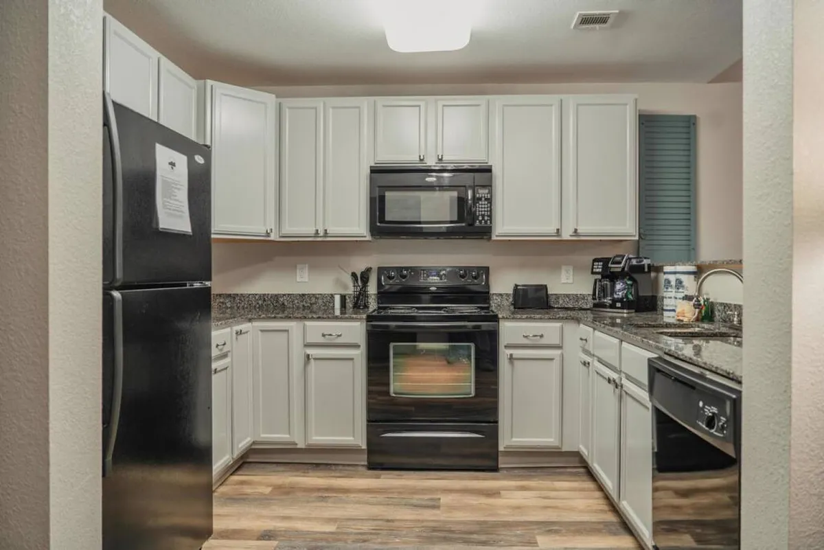 This image features a kitchen with black appliances, granite countertops, and crisp white cabinetry. The space is well-lit and organized, with ample counter space for meal prep and entertaining, reflecting a modern, functional environment ideal for cooking and gathering.