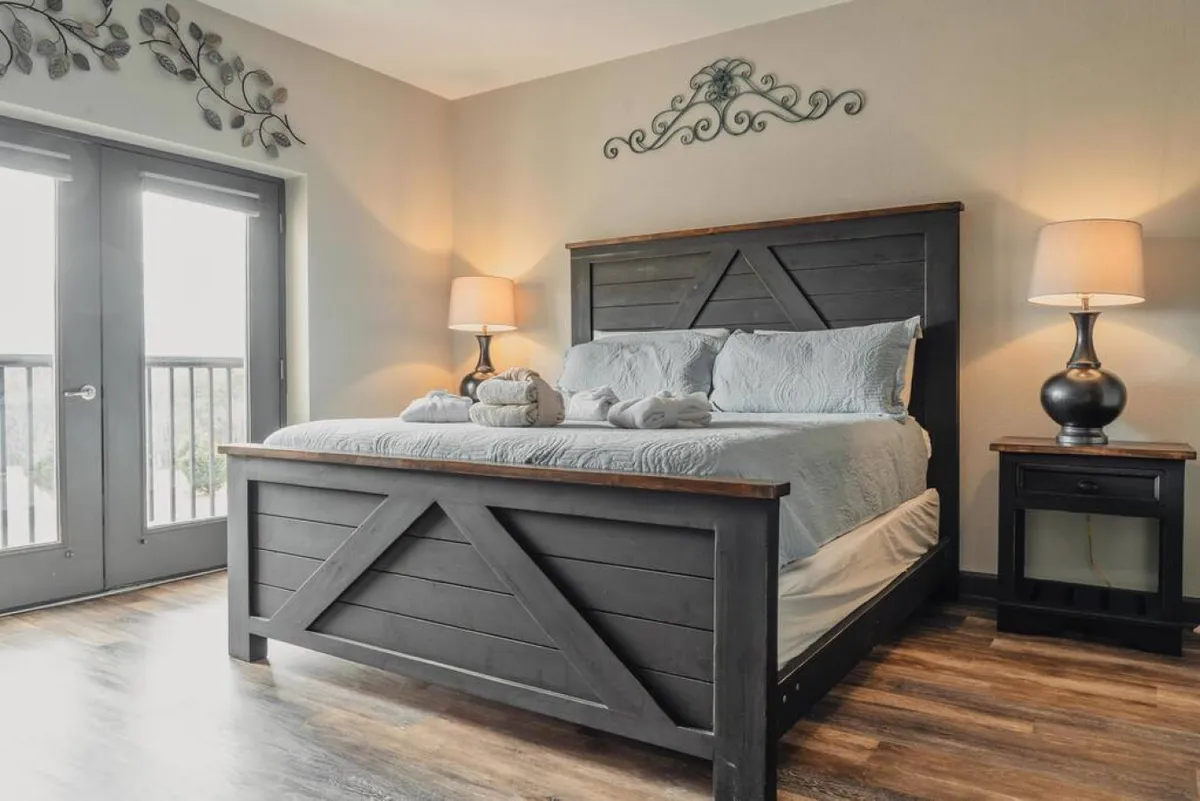 A beautifully styled bedroom with a plush bed adorned with decorative pillows, flanked by softly glowing bedside lamps. Expansive windows reveal a scenic view, inviting natural light and offering a glimpse of the serene mountain surroundings.