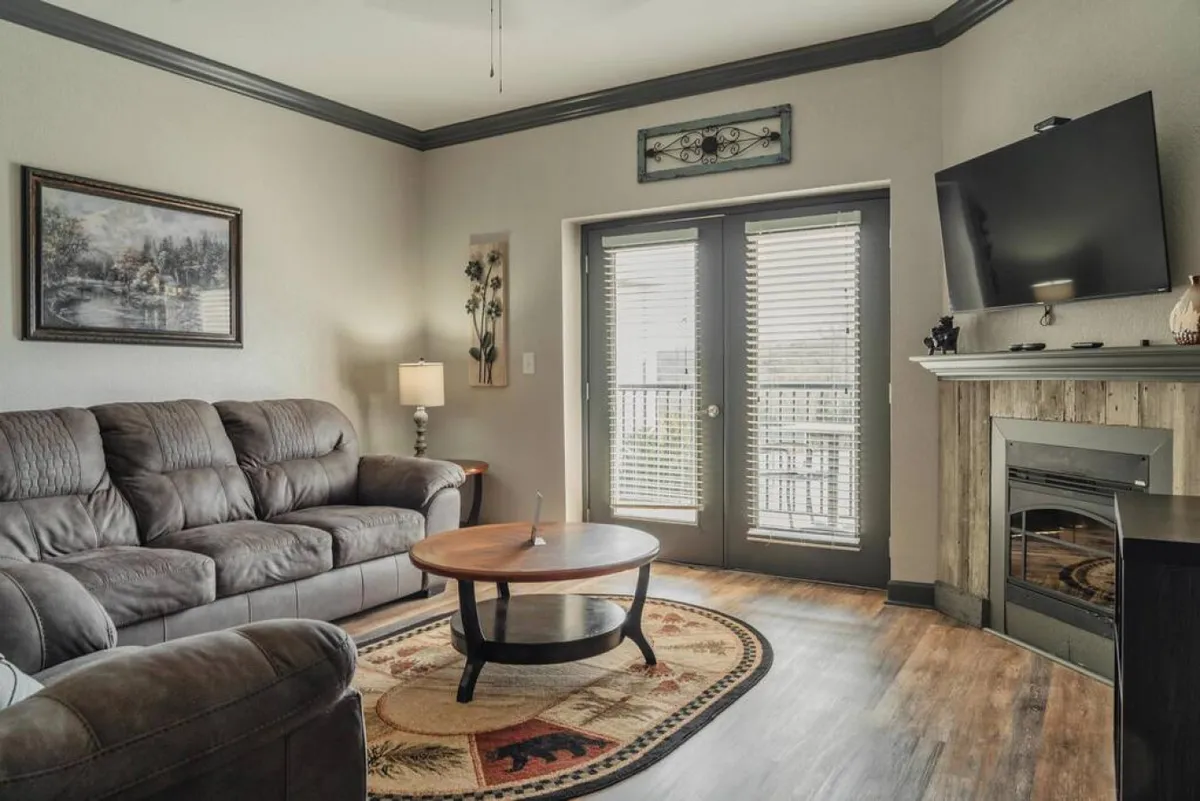 A welcoming living space with a sofa, coffee table, TV, fireplace, and double doors that likely lead to an outdoor patio or balcony. The setup suggests a cozy spot to unwind after experiencing the nearby attractions.