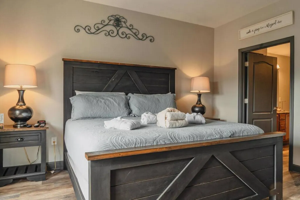A view of a neatly made bed with inviting nightstands on each side, soft lighting, and tasteful wall decor. Towels are arranged on the bed, and the overall palette and design evoke a sense of calm and comfort, perfect for relaxation and restful sleep.