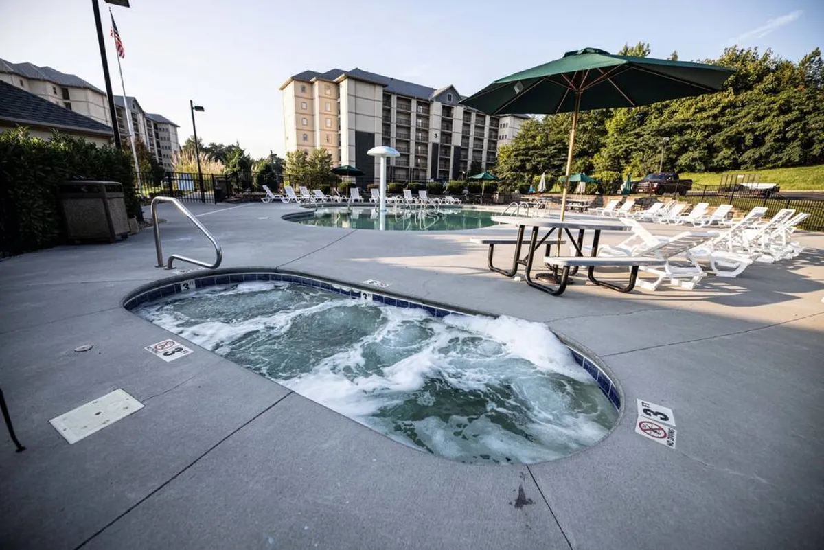 A cheerful scene featuring both the hot tub and the swimming pool, with lounge chairs and a picnic table nearby. The setup is ideal for socializing, relaxing, or unwinding after a day of activities. The atmosphere is bright and family-friendly.