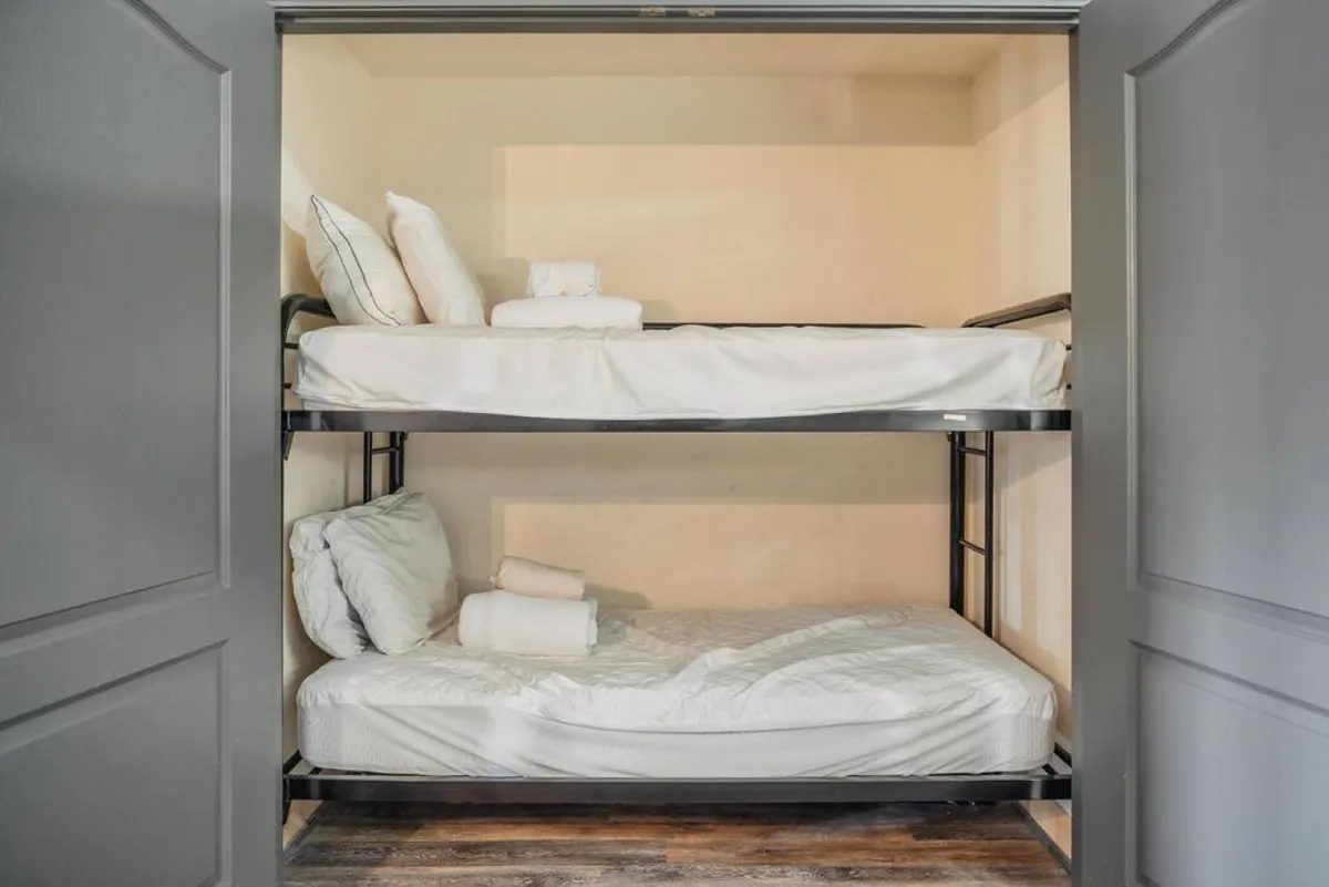 A close-up view of a 'bunk closet' featuring twin bunk beds with neatly arranged bedding and textured pillows. The space exudes warmth and intimacy—ideal for children or guests seeking a playful sleepover nook.