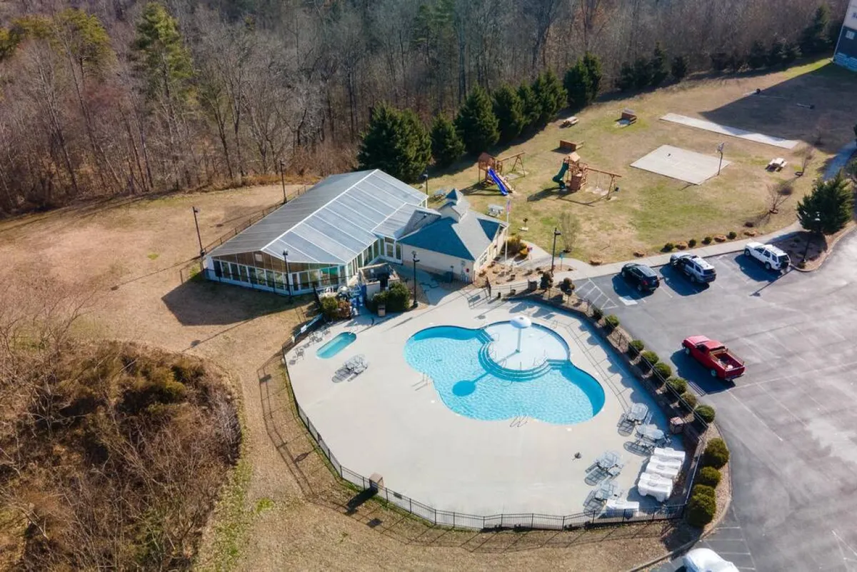 An outdoor recreational area with a sparkling swimming pool, sun loungers, and a nearby playground set against the backdrop of the property’s building structure. The scene is lively and family-friendly, highlighting spaces for both swimming and children's play.
